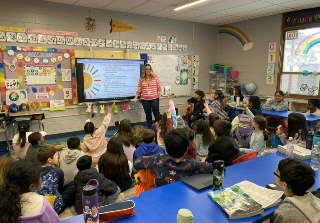 teacher standing by a promethean board in front of a class of students 